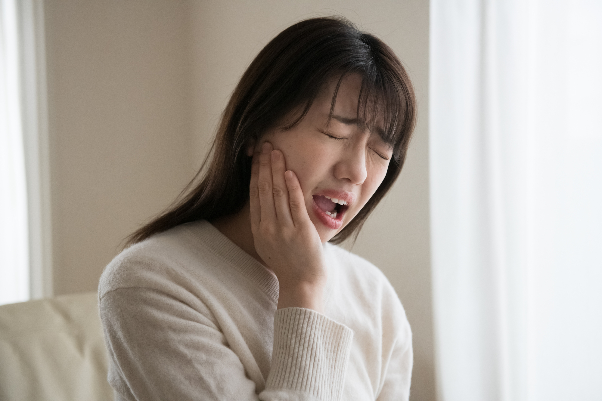 頬を押さえて歯の痛みに苦しむ女性のイメージ│歯の怪我の治療なら、瀬戸歯科